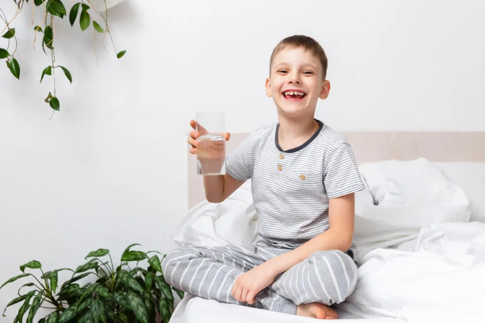 ieťa sediace na posteli s pohárom vody počas oddychu pri prechladnutí a kašli