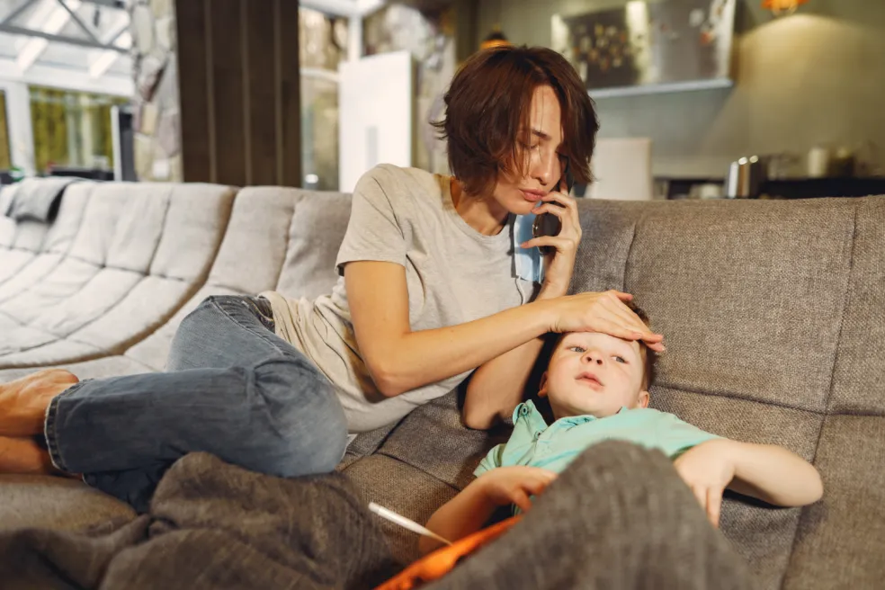 Mama telefonuje o pomoc pri chorom dieťati ležiacom na pohovke s príznakmi zhoršeného zdravotného stavu