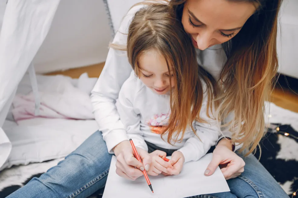 Mama pomáha dcére pri domácom písaní do zošita. Spoločne precvičujú diktáty pre 3. ročník základnej školy, vybrané slová a slovenský pravopis.